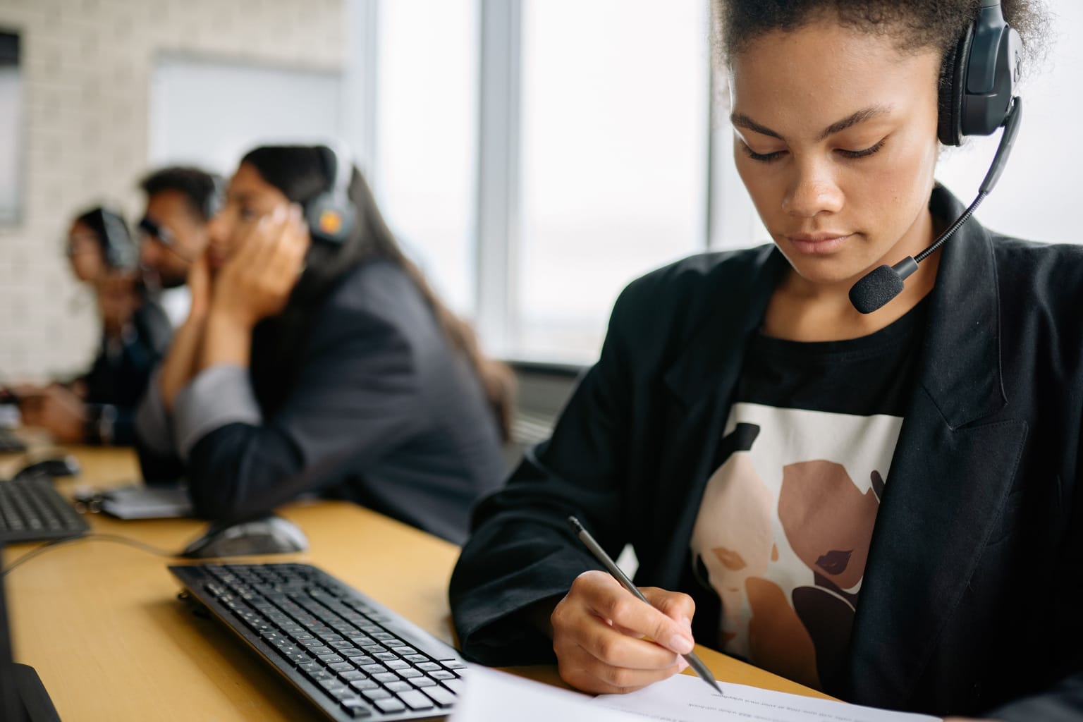 AI receptionist vs answering service: an answering service agent in a headset taking notes, with colleagues on calls behind her