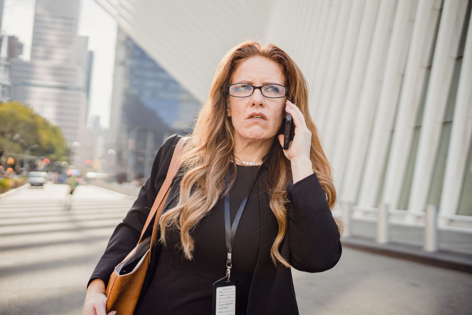 A businesswoman with an ID lanyard taking a call on a city street