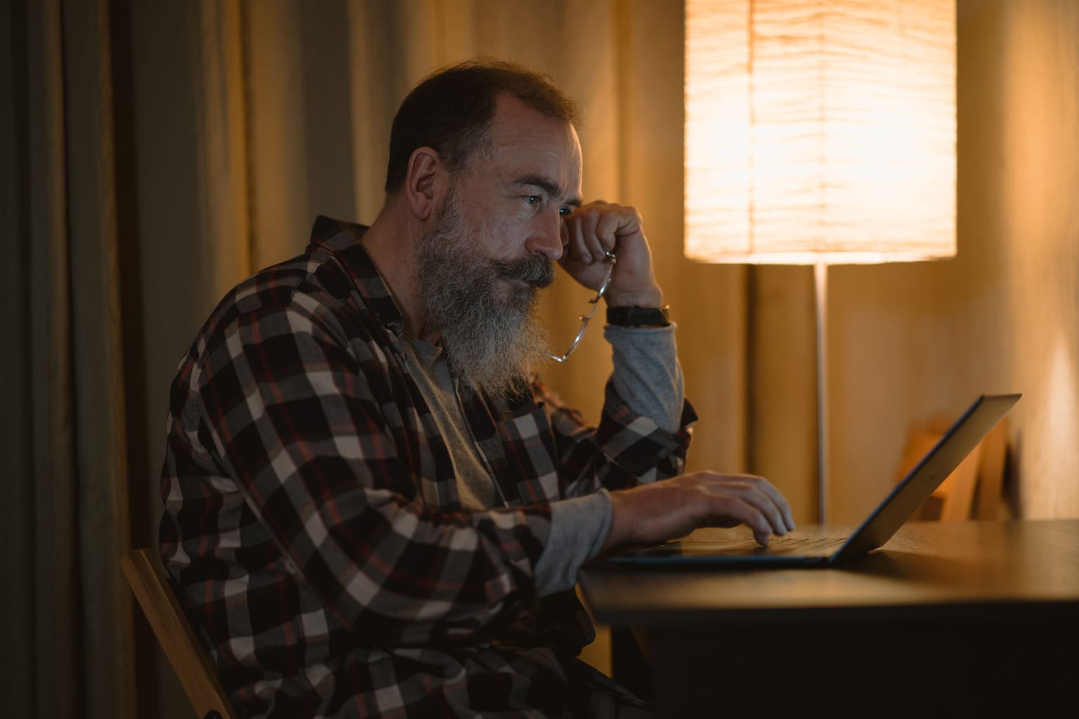 A man typing on his laptop at home in the evening by lamplight