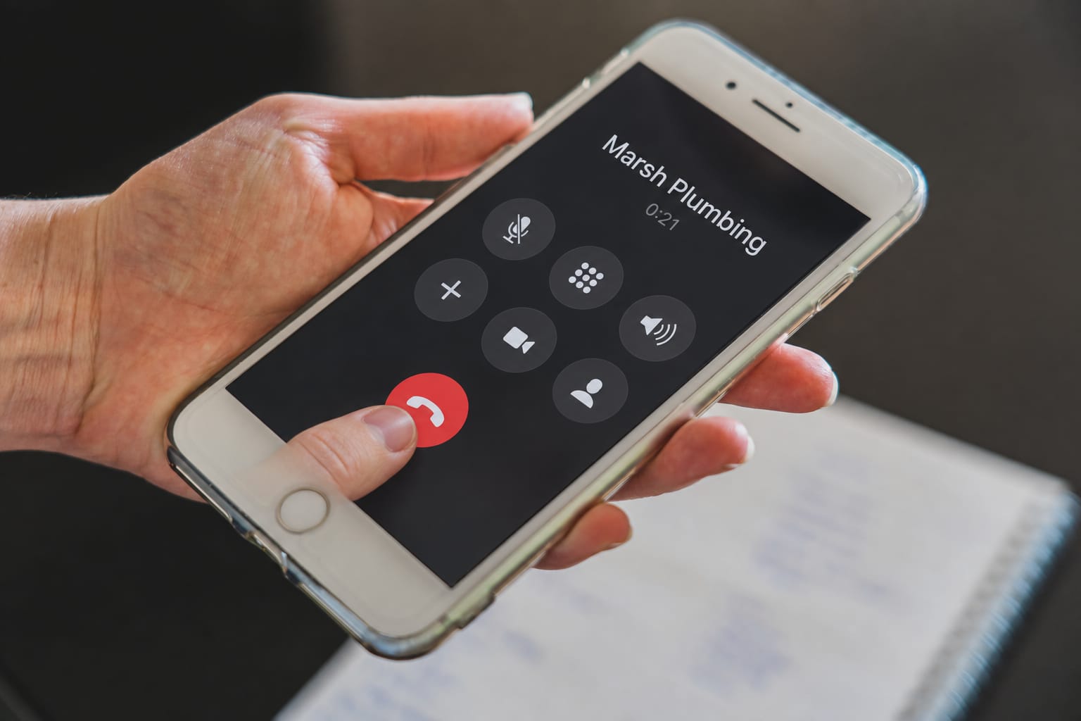 A caller's finger on the end-call button during a call to a plumber