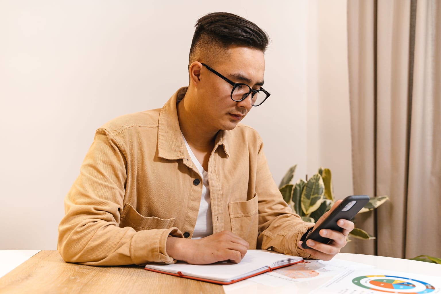 A man at his desk checking his phone and writing a tally in a notebook