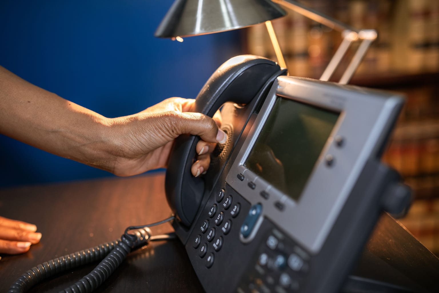 A hand picking up the handset of an office desk phone
