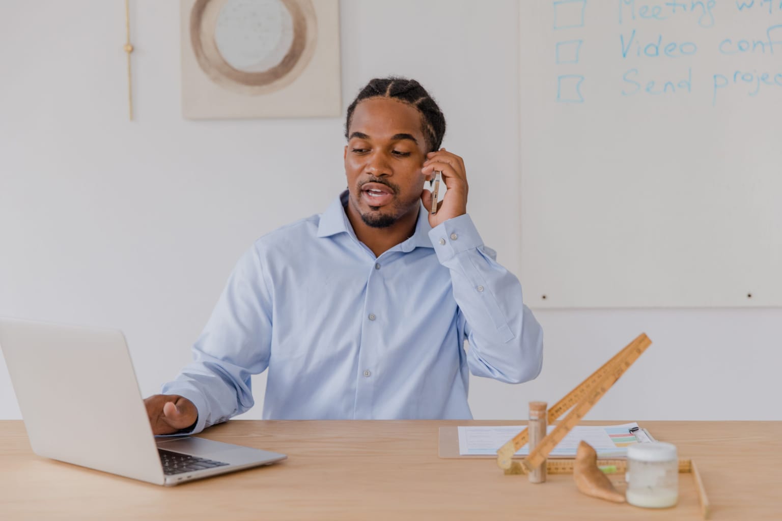 A man at his desk taking a phone call beside his laptop
