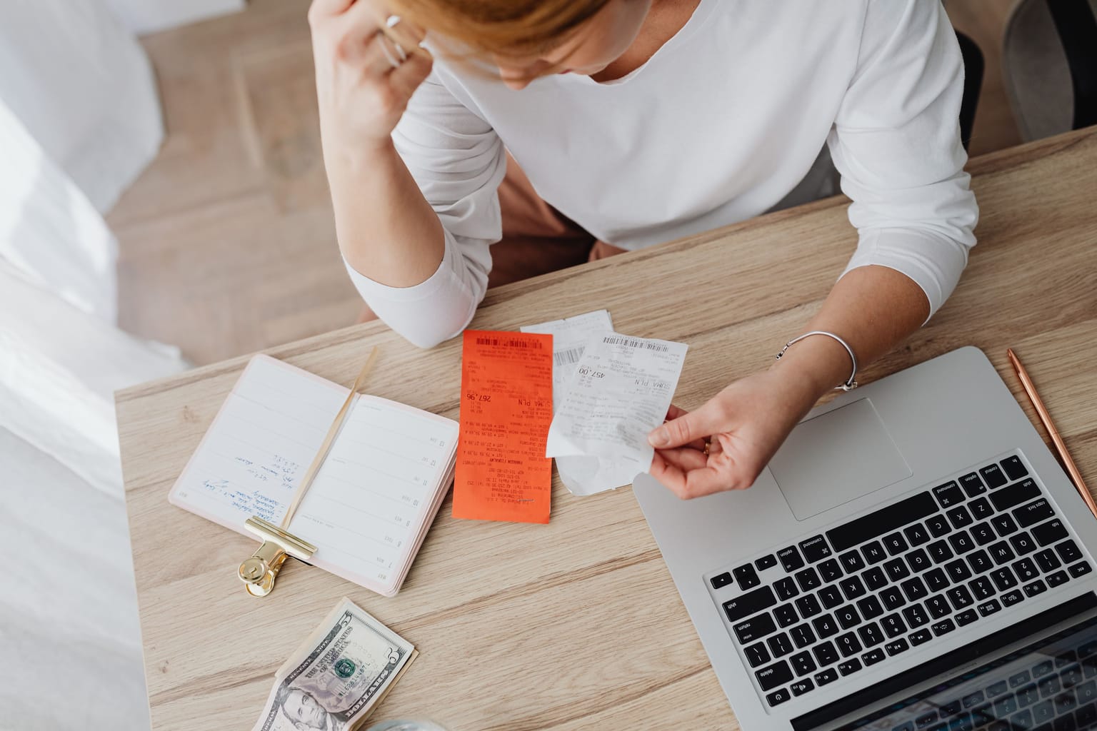 A business owner at her desk with a hand to her head, going through receipts beside her laptop