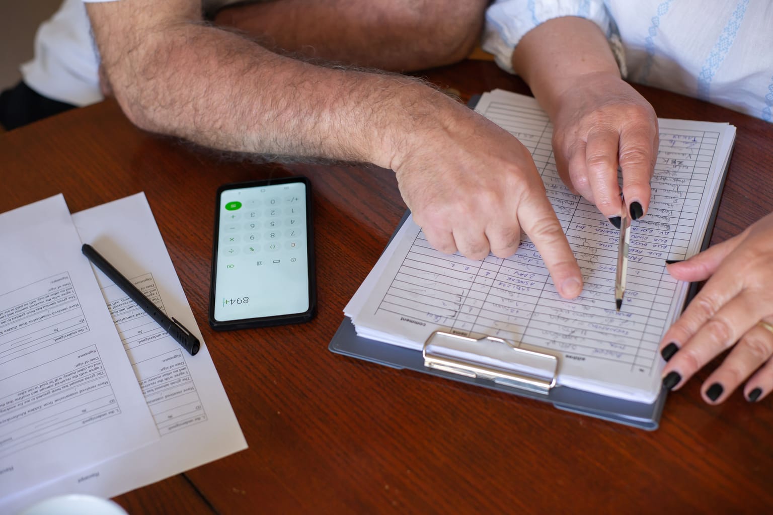 Hands working through a table of figures on a clipboard with a phone beside it