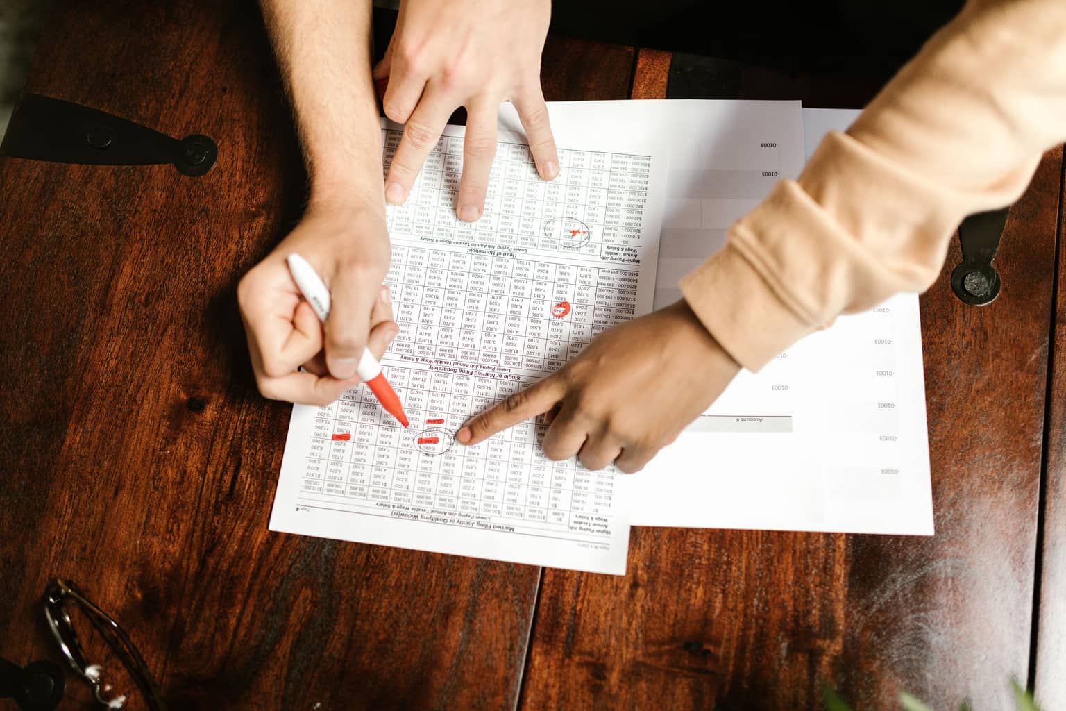 Two people going through a printed statement line by line with a red pen