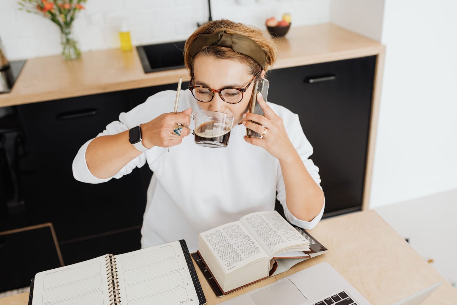 A woman on a phone call at her kitchen table with a planner open in front of her