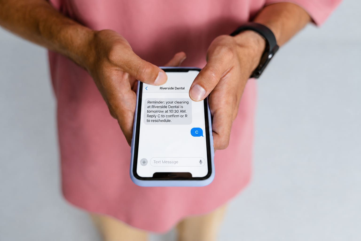A phone showing a text from the practice: your cleaning is tomorrow at 10:30 AM, reply C to confirm or R to reschedule. The patient has replied C.