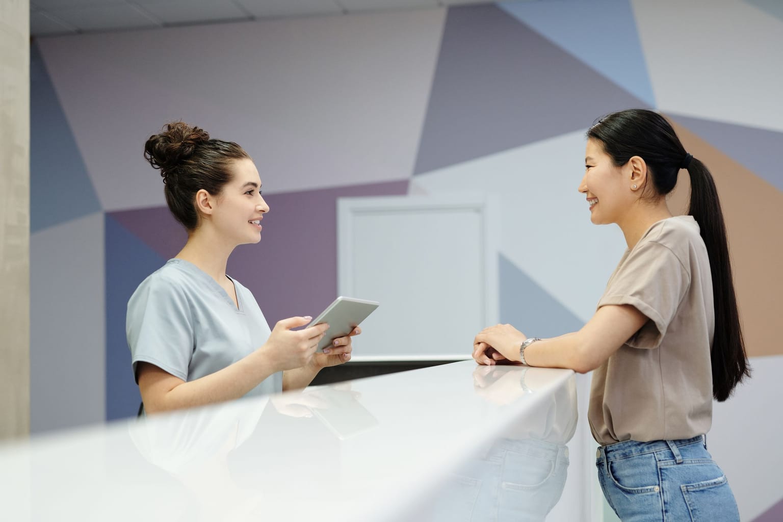 How to reduce missed calls at a dental office: a front desk team member in scrubs helping a patient at the counter