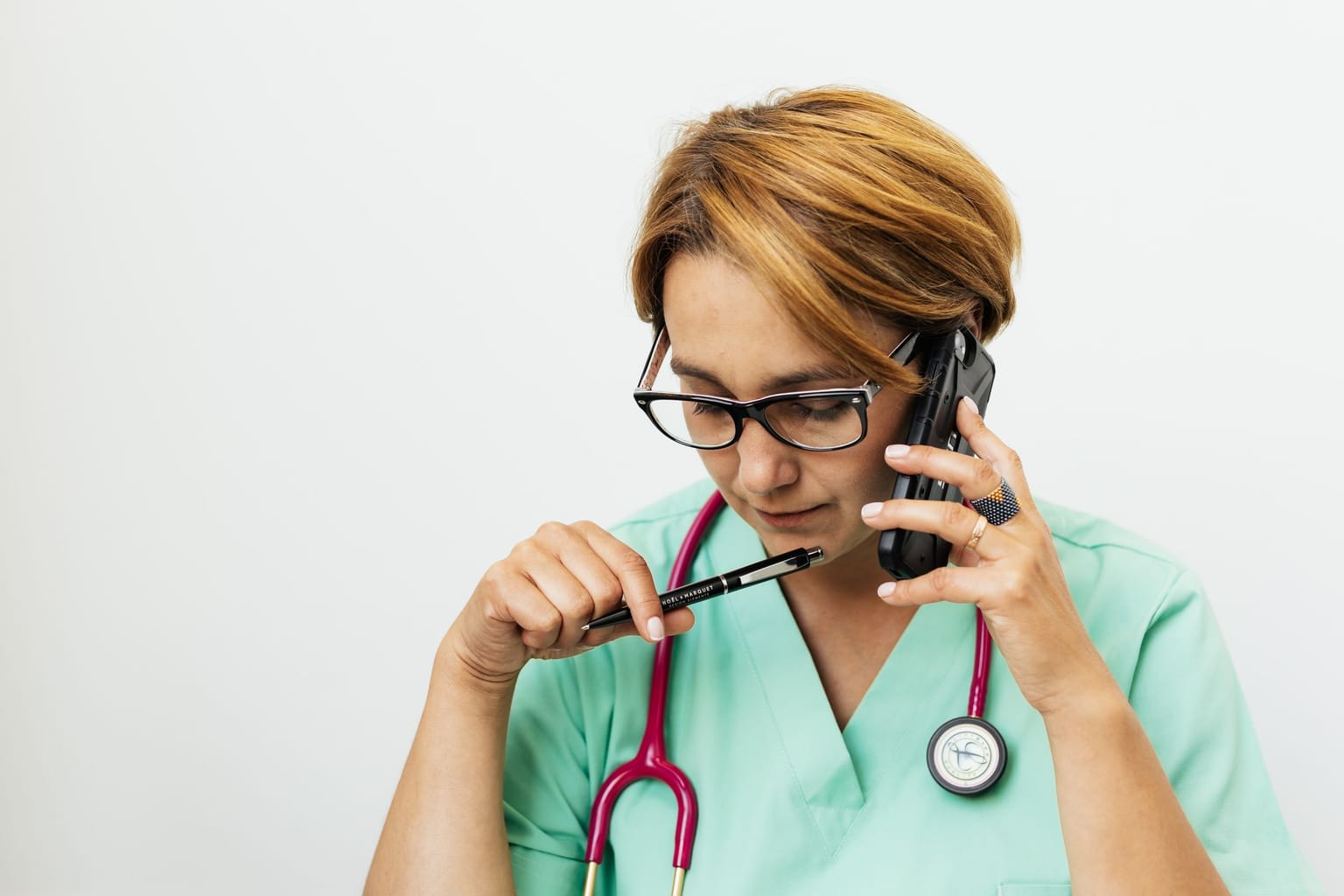 A clinician in scrubs with a stethoscope listening closely on a phone call