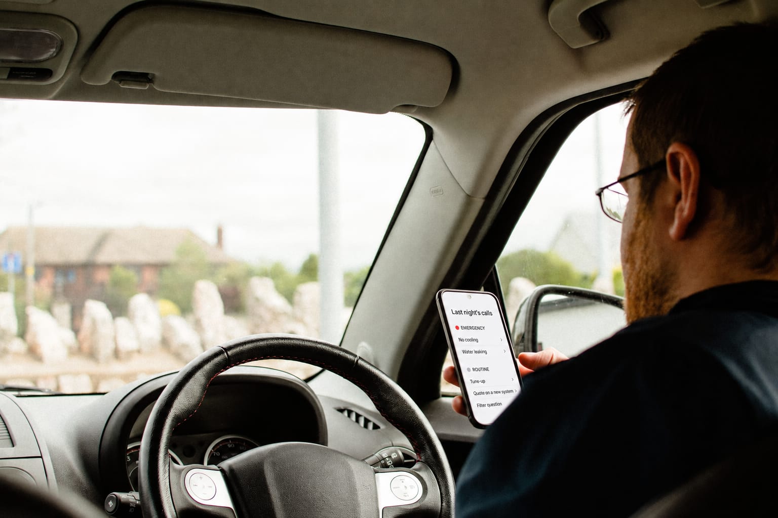 A technician in the driver's seat with his phone showing last night's calls sorted into emergency and routine