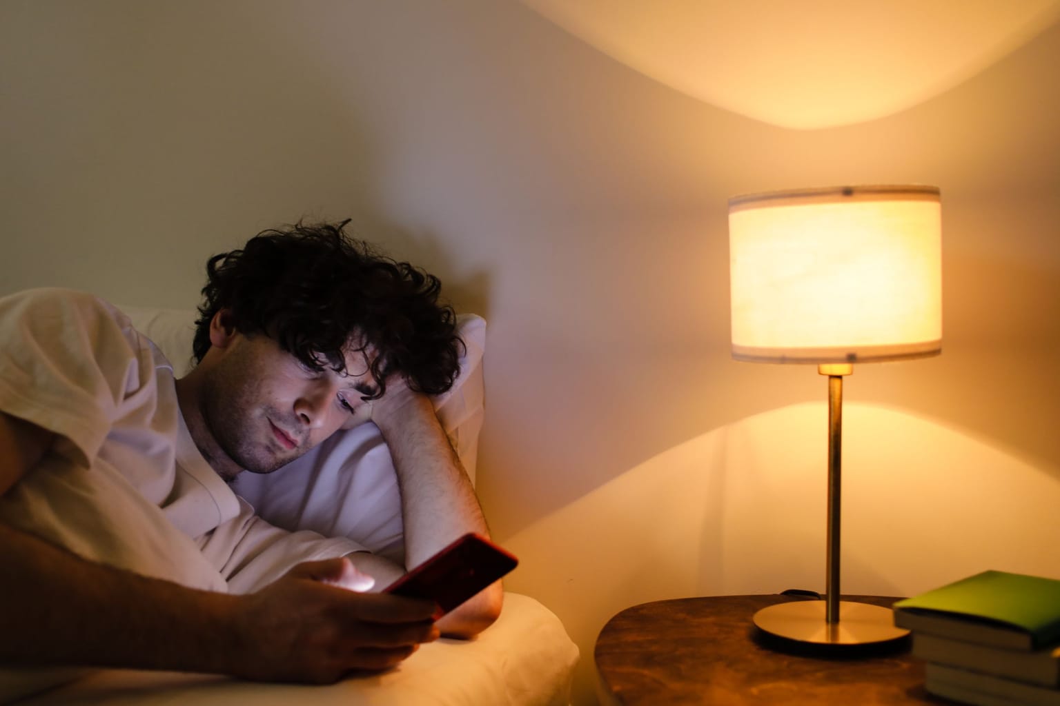 A man in bed at night checking a call on his phone by lamplight