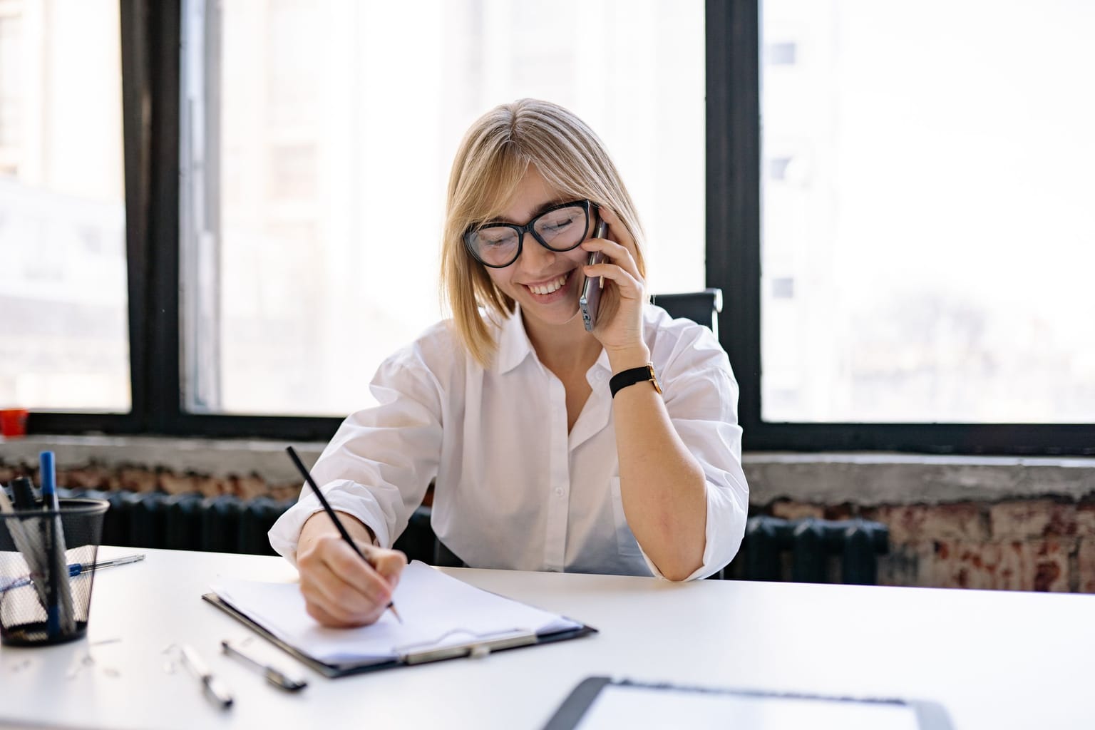 A woman taking notes while on a phone call at her desk