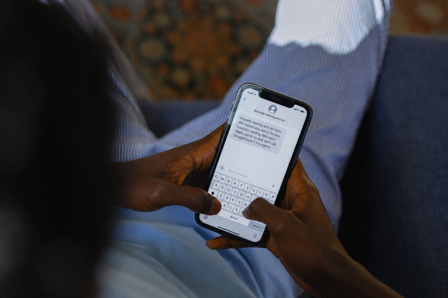 Hands on a phone showing a missed-call text: Bayside Heating and Air here. We missed you, sorry. Do you have any cooling right now? Reply yes or no.