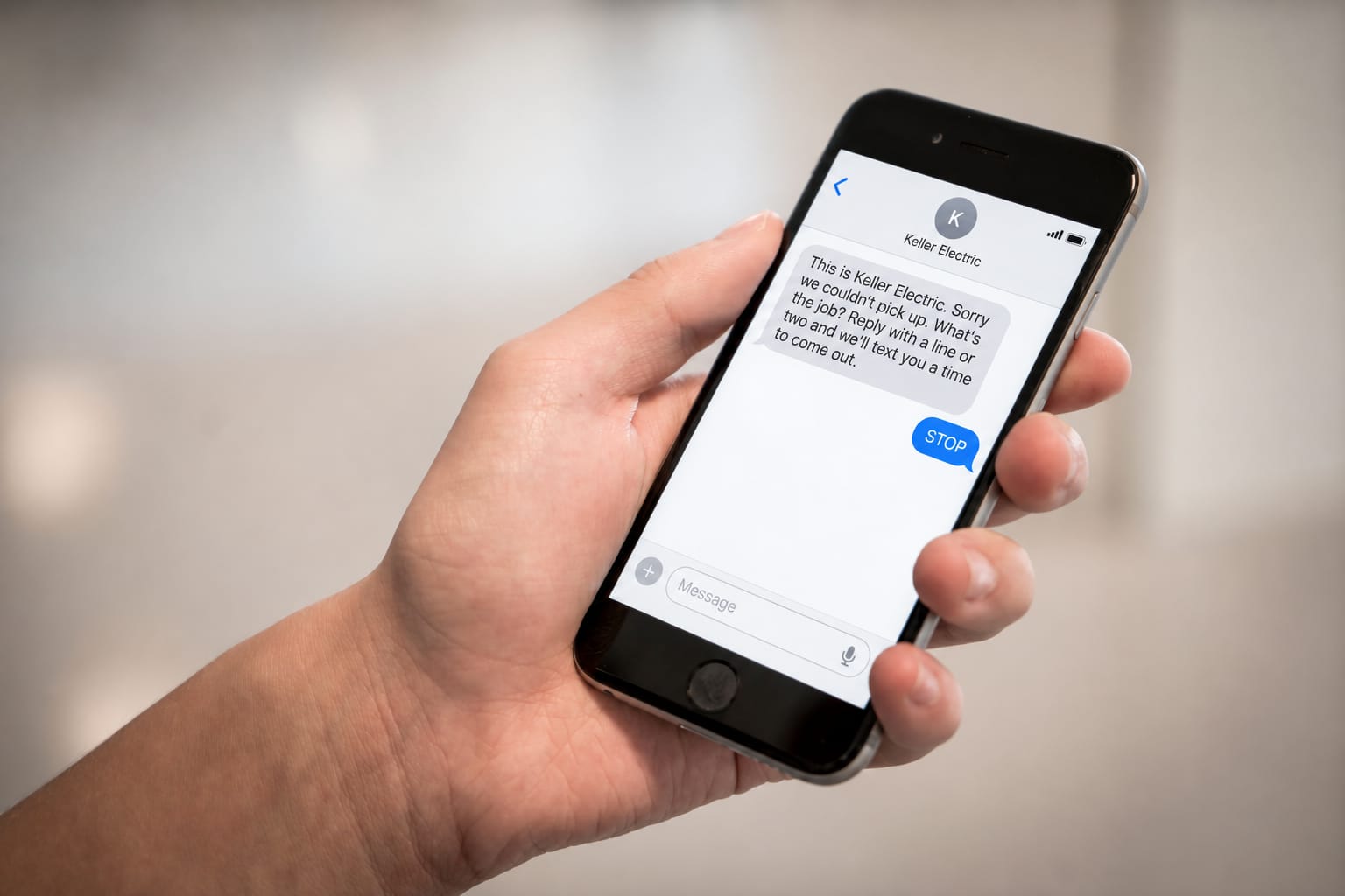 A hand holding a phone showing a text thread in which the last reply is STOP