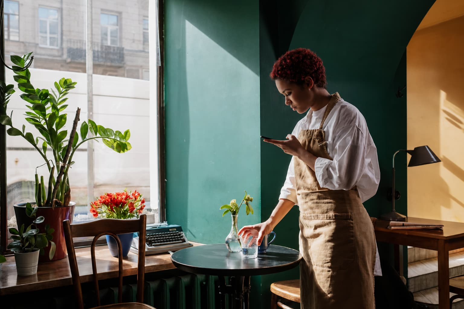 Responding to positive reviews: a cafe worker reading her phone while setting a table by the window