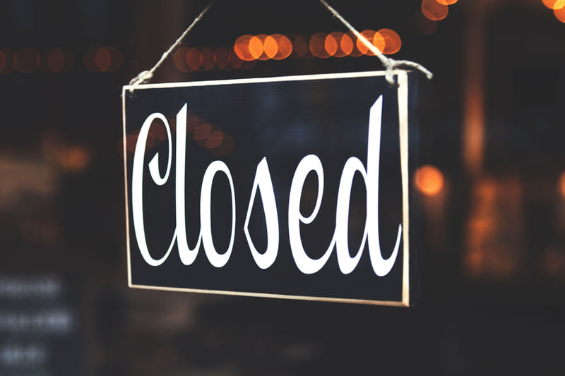 A Closed sign hanging in a shop window at night, street lights blurred behind it.