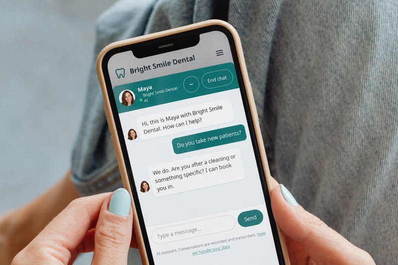 A phone showing a dental practice website with the chat window open. A visitor asks: Do you take new patients? Maya answers: We do. Are you after a cleaning or something specific? I can book you in.