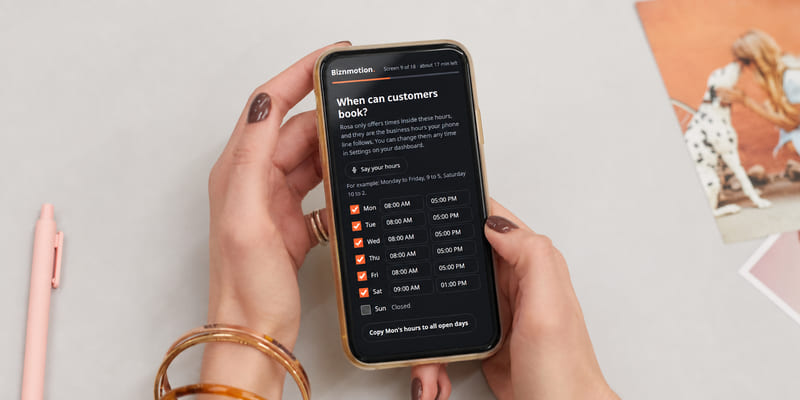 Hands holding a phone on the setup form screen When can customers book?, with opening hours for each day.