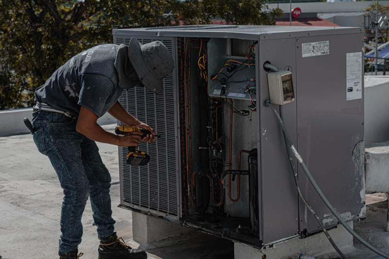 A technician bent over an open rooftop air conditioning unit with a tool in hand.